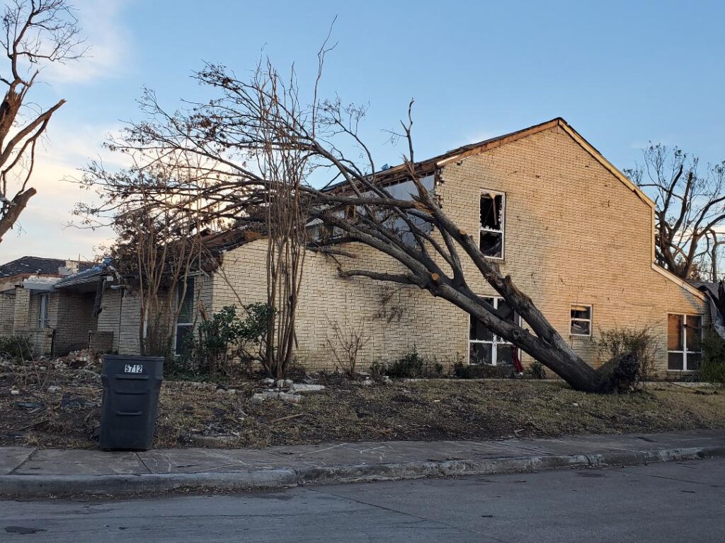 This two-story brick house has a tall tree that was uprooted and fell against the house during a major Texas storm.