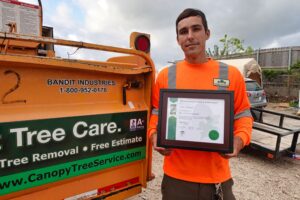 Lucas Rumancik, Certified Arborist, hold Certification Plaque next to a chipper.